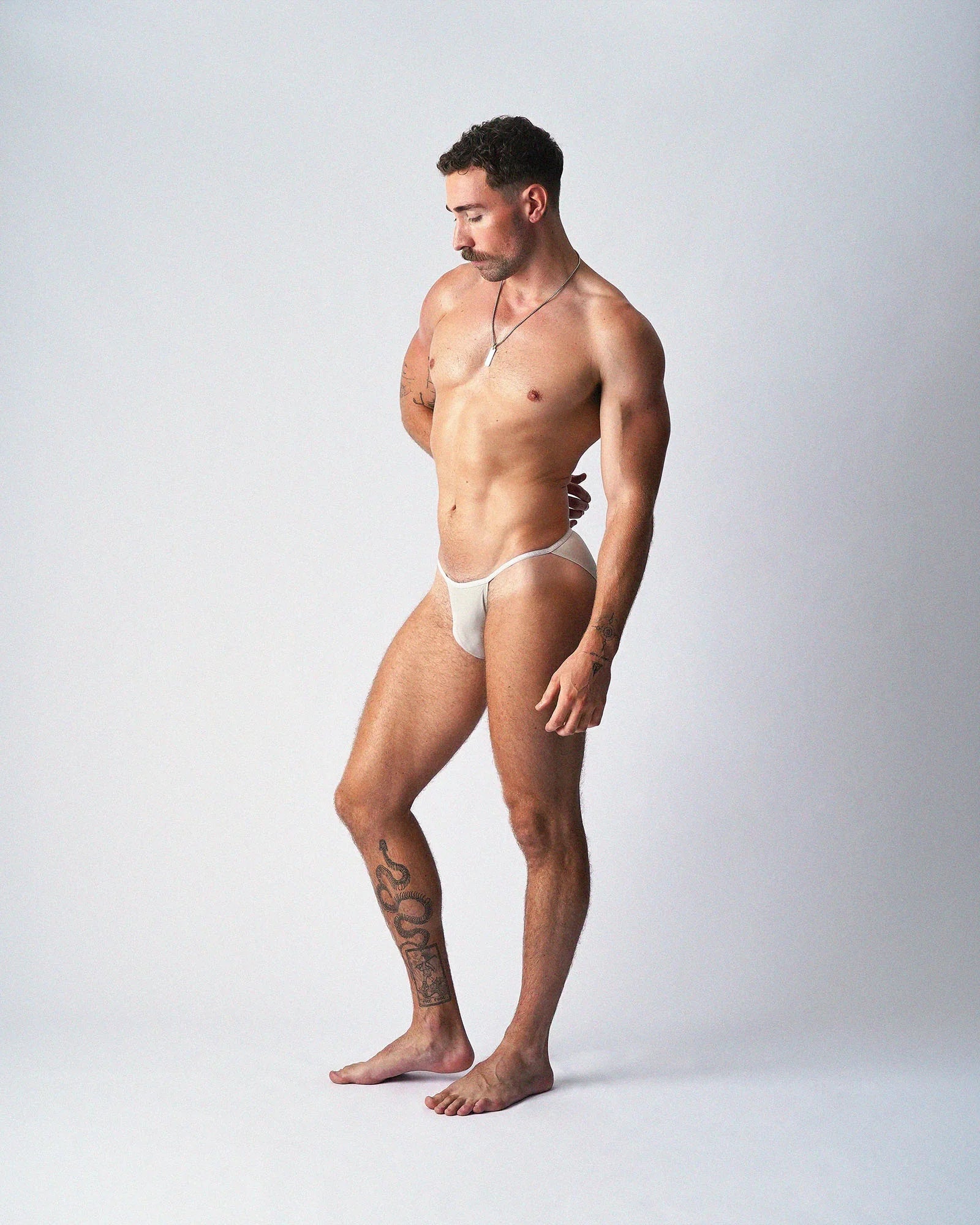 A man modeling teamm8 Glide Micro Brief in off-white, standing against a grey background.