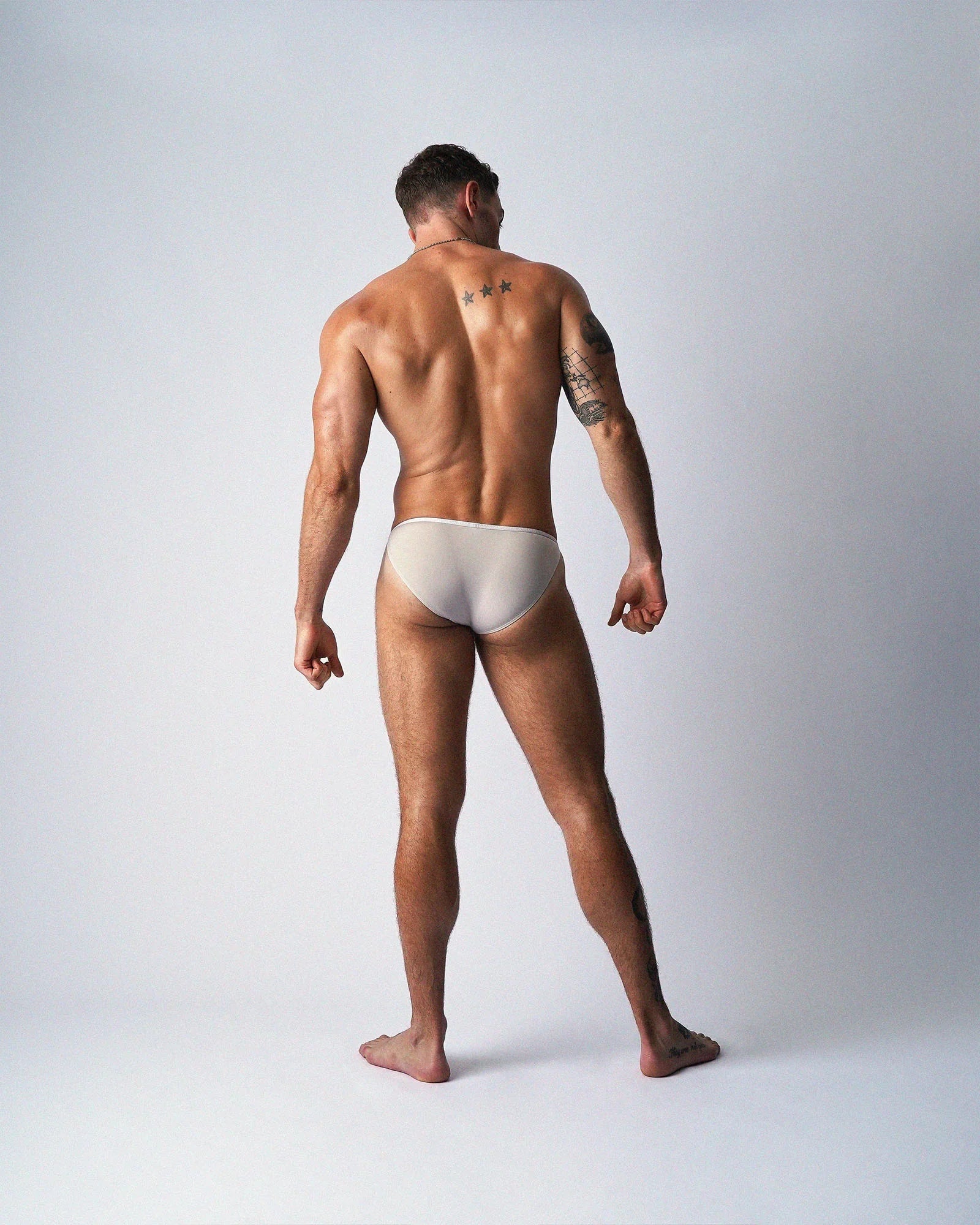 Rear view of a man wearing teamm8 light grey Glide Micro Briefs against a plain white studio background.