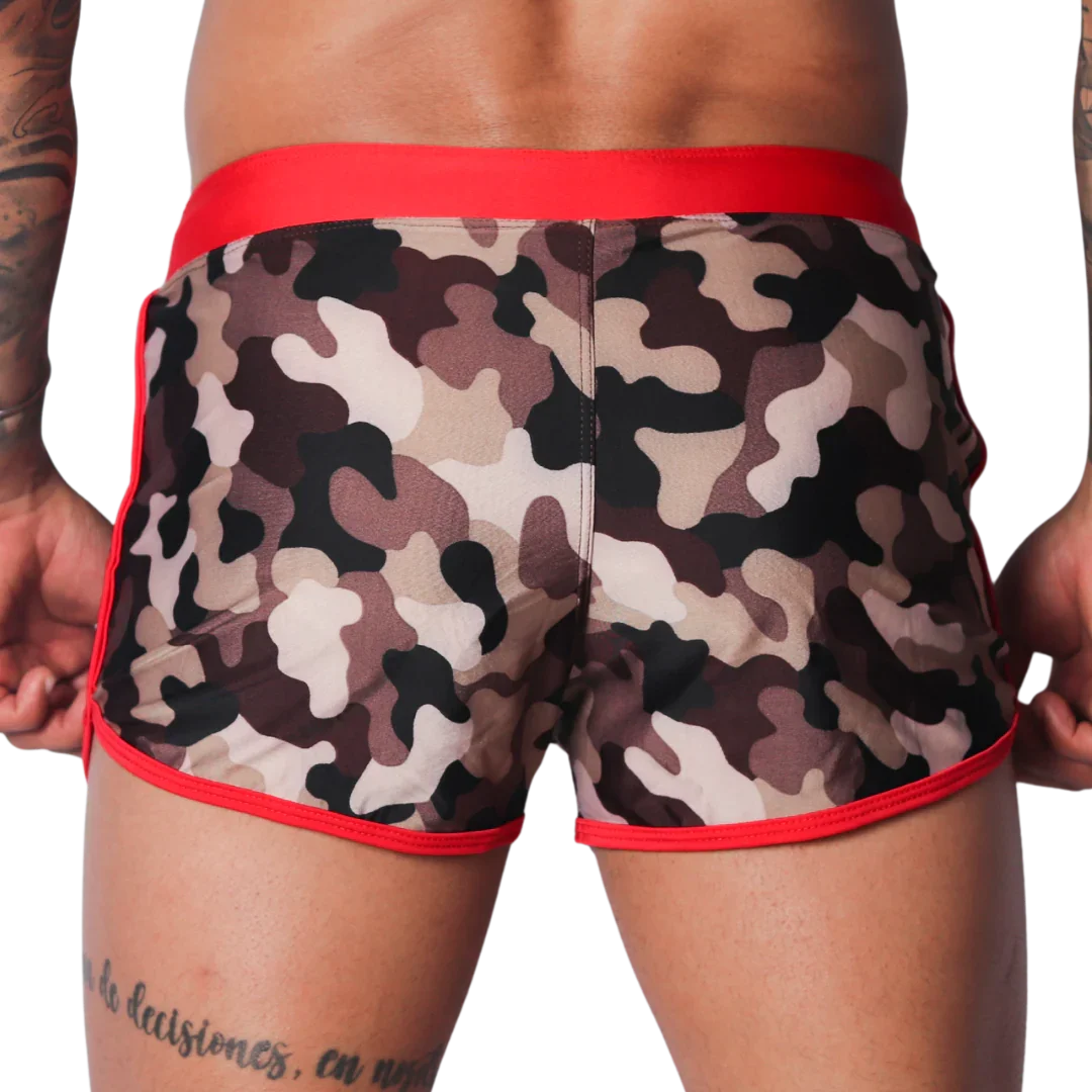 Short camo-print swim trunks with a wide red waistband and red piping trim along the leg openings.