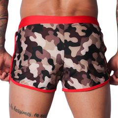 Short camo-print swim trunks with a wide red waistband and red piping trim along the leg openings.