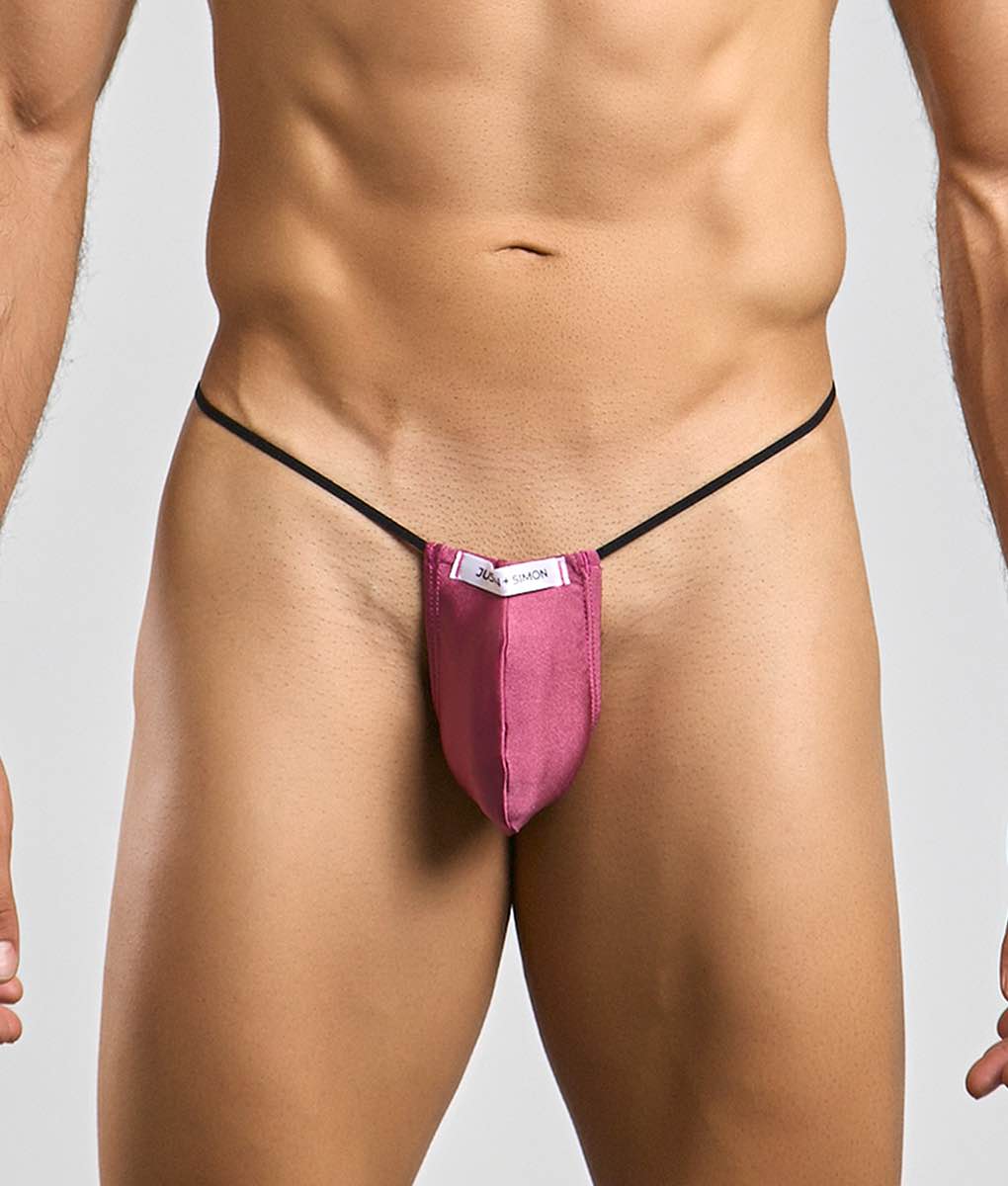 A vibrant pink form-fitting thong g-string with black elastic straps and a white Justin Simon classic brand tag