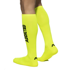 Bright neon yellow knee-high socks with black addicted lettering and a small foot logo in the product addicted neon socks