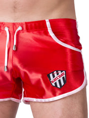 Red satin swim trunks with white drawstrings and trim featuring a black and white barcode logo patch size xl