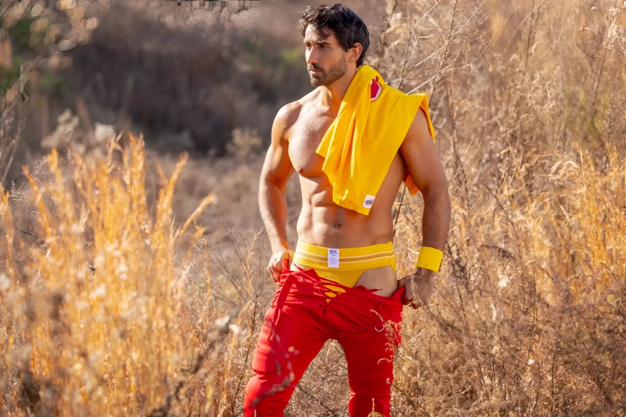 A man wearing bright red athletic pants with yellow trim and a yellow bike athletic jockstrap draped over shoulder
