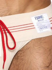 Beige bike brand swim trunks with red drawstring and trim shown with vintage cream bike athletic lace-up jockstrap