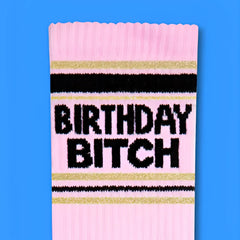 Pink knit birthday bitch crew socks with black and gold stripes featuring bold black lettering for birthdays