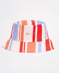 A vibrant cabana bucket hat with bold red blue and cream vertical stripes and subtle gold embroidered logo on front