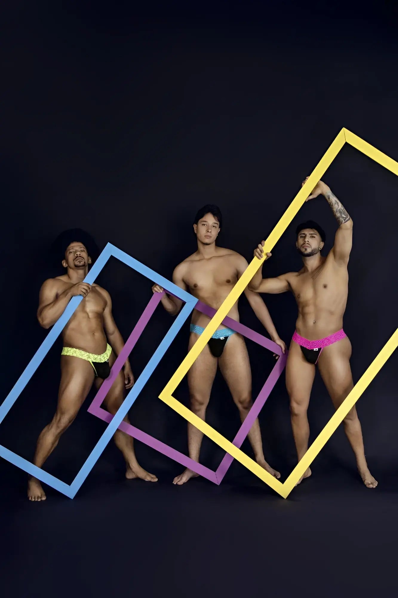 Three men pose with colorful oversized frames in front of a dark background featuring candyman 99370 blue lace thongs