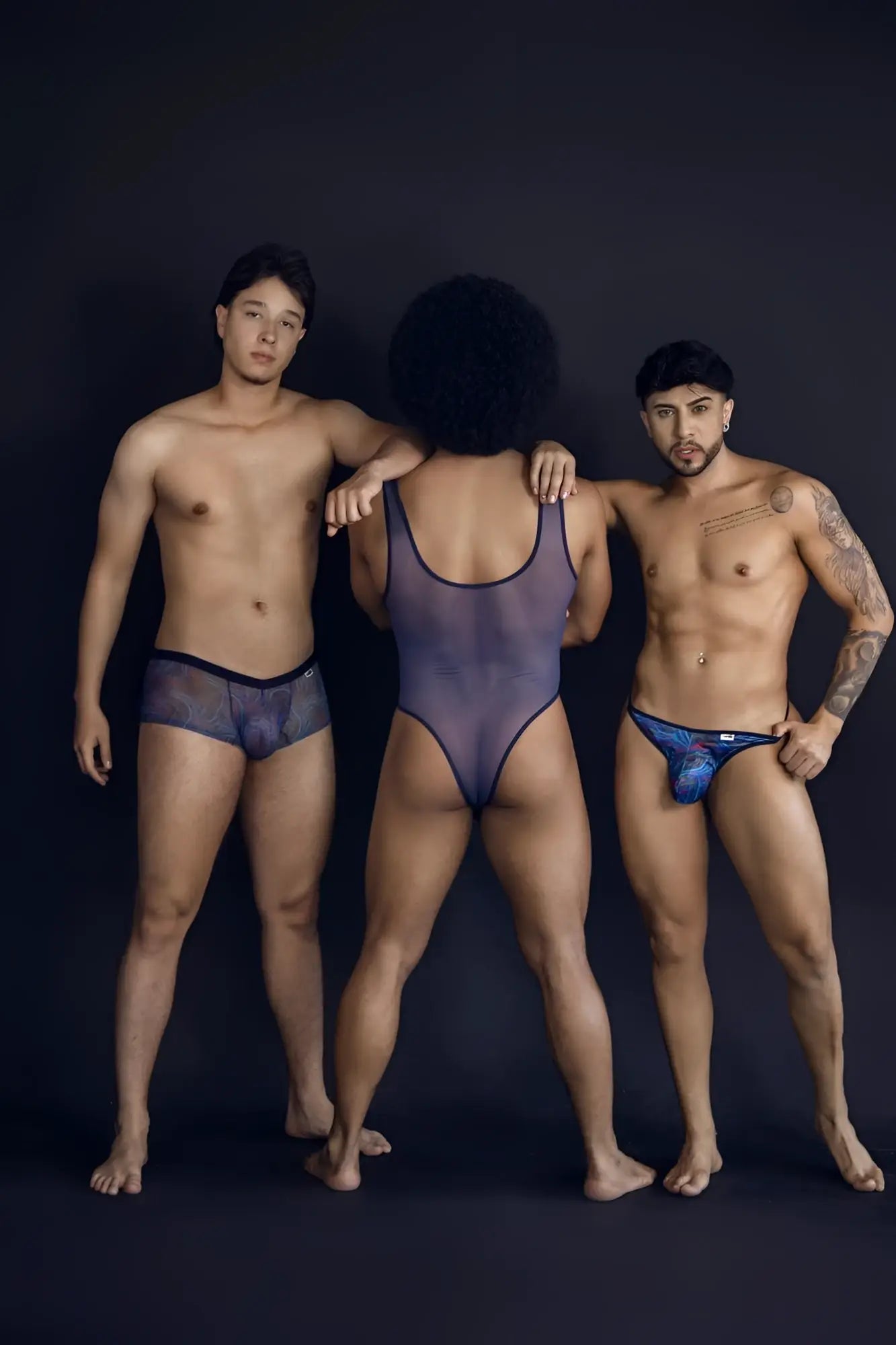 A sheer dark purple one-piece bodysuit with black trim featured alongside candyMan 99873 multicolor seawater trunks