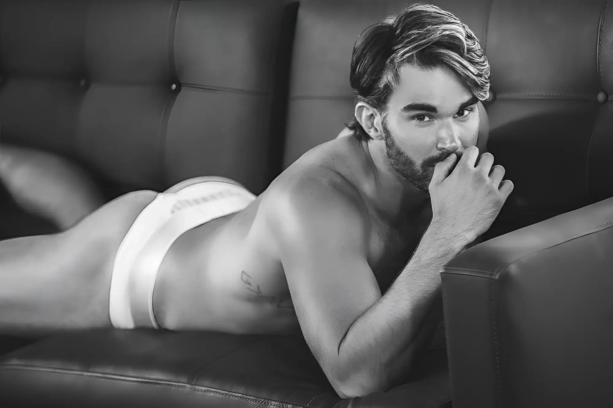 A man lying on a couch wearing white clever 1034 lucerna thong briefs showing the front side