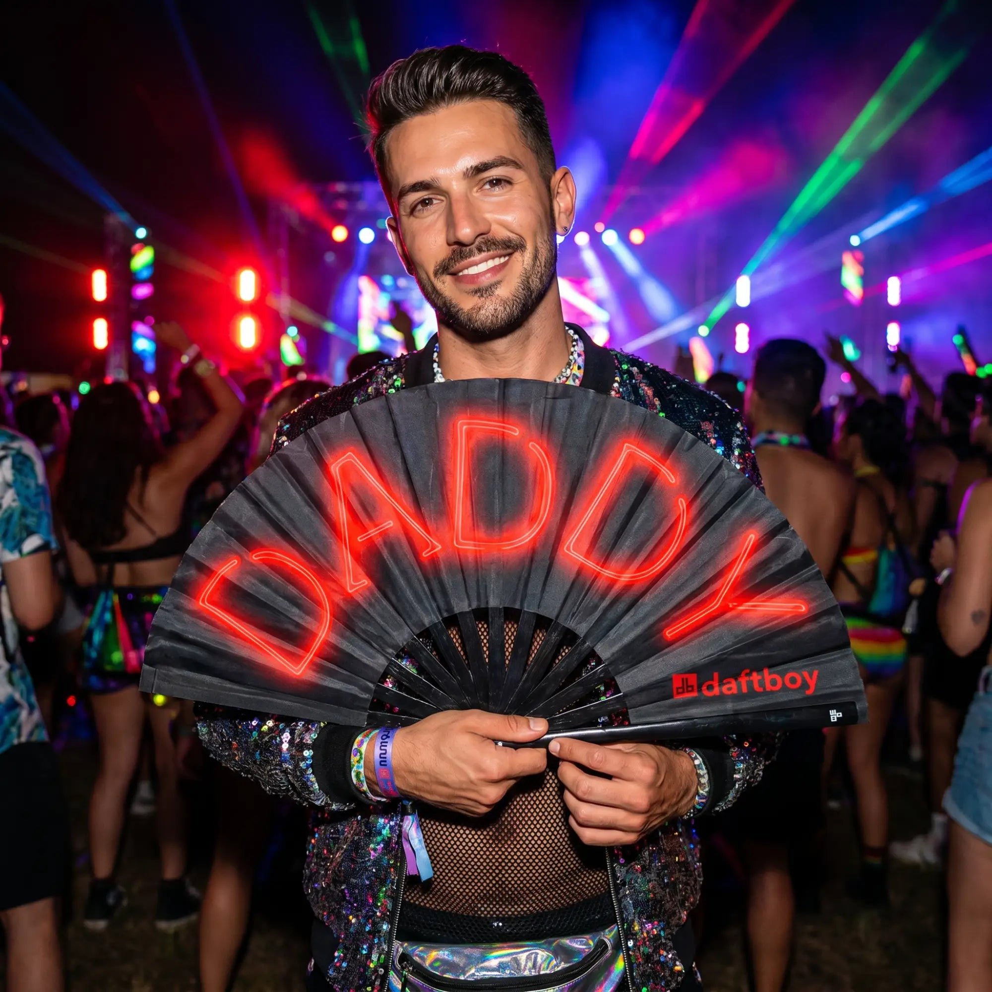 Stylish man at pride festival holding Daftboy Lit Daddy black bamboo fan open, red neon DADDY text, colorful crowd