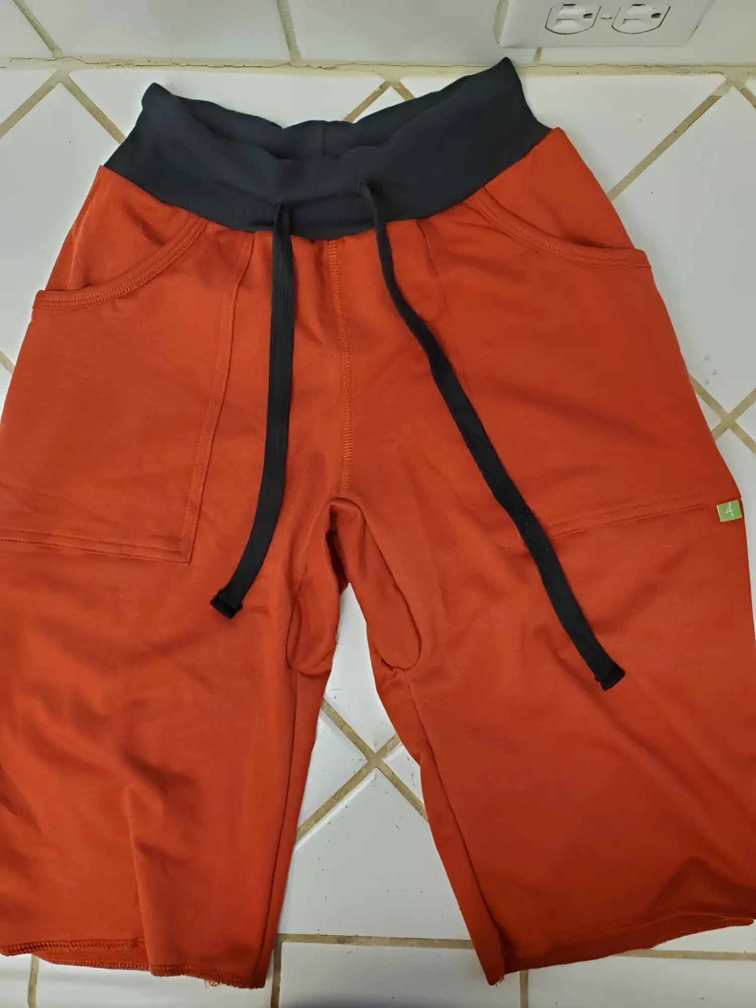 Eco-Track short cinnabar orange athletic shorts with black waistband, drawstrings, side pockets, and green brand tag