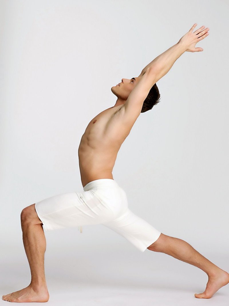 A man wearing white eco-track short yoga shorts in a dynamic stretching pose highlighting form-fitting comfort