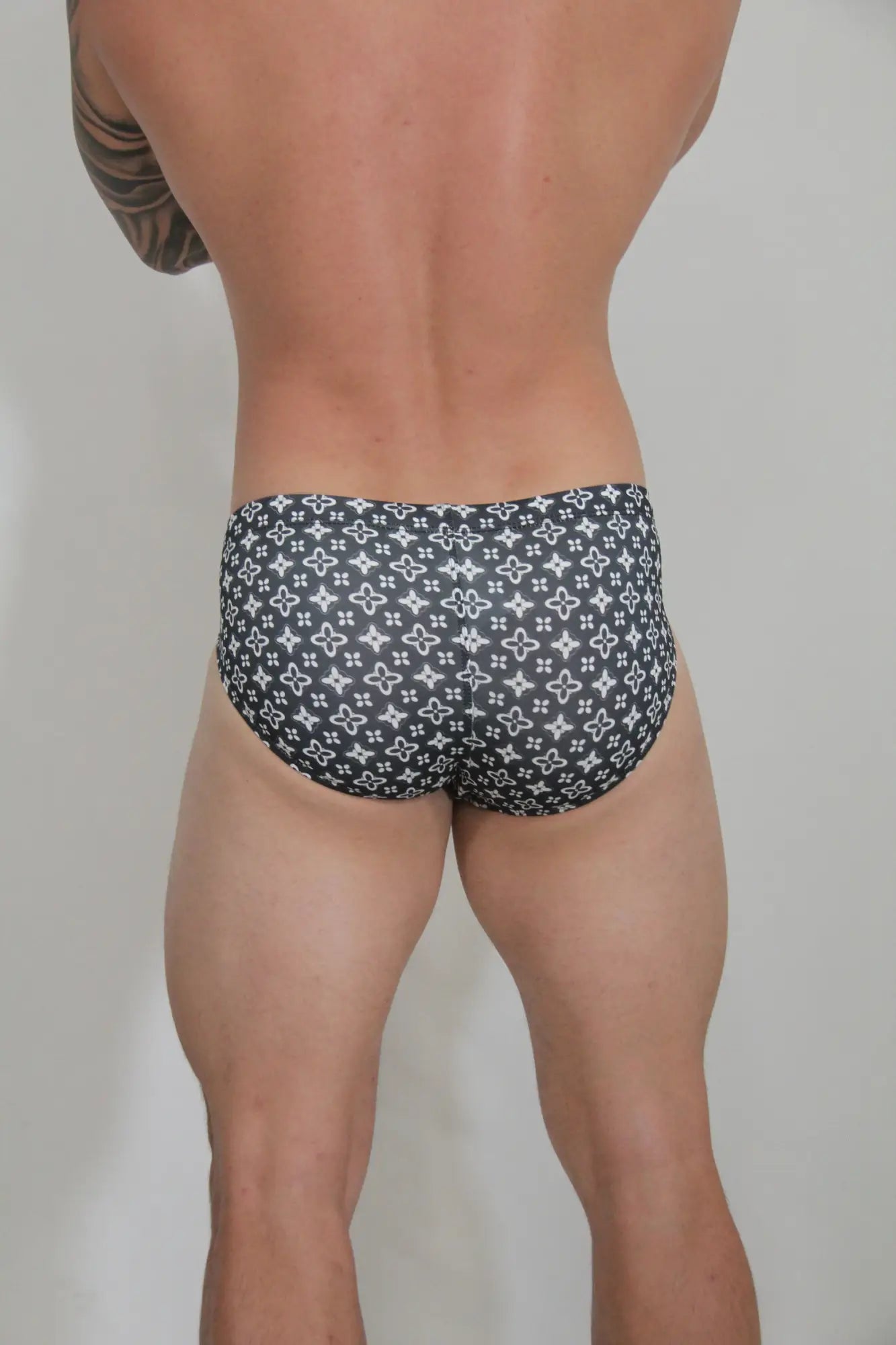 Black swim brief with a repeating white monogram pattern designed for stylish beachwear use