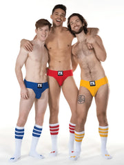 Three men wearing brightly colored low-rise briefs with black fk logo and fk sport white tube sock striped socks