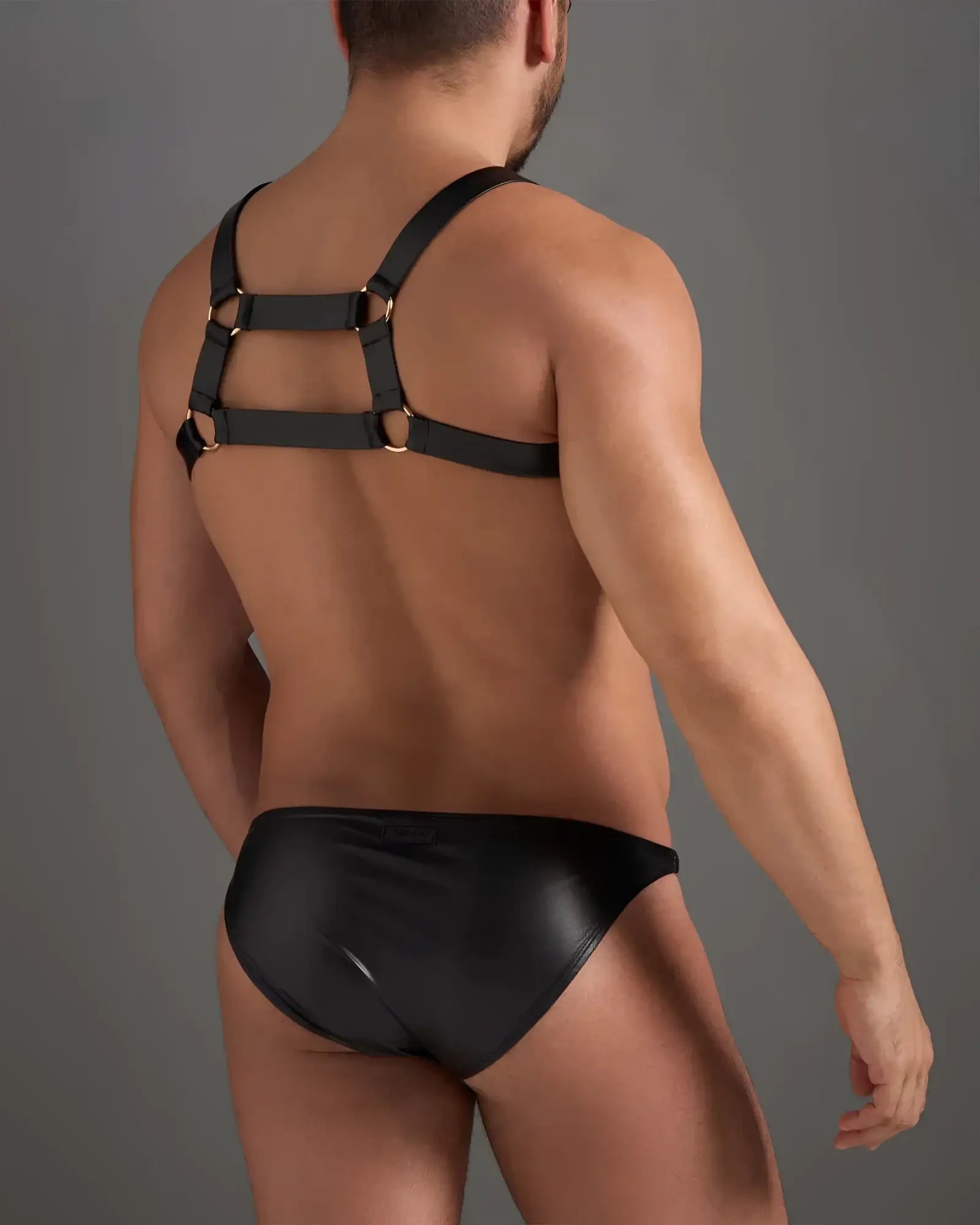 Black leather flex harness with gold-toned metal rings worn over matching black patent leather brief front view
