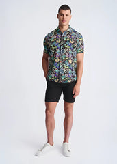 A man wearing a floral lightweight linen tencel short-sleeved shirt with a multicolored pattern on a dark background
