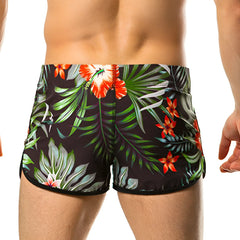 Black swim trunks from Gigo Garden Beachwear with vibrant orange hibiscus flowers and green palm leaves tropical print