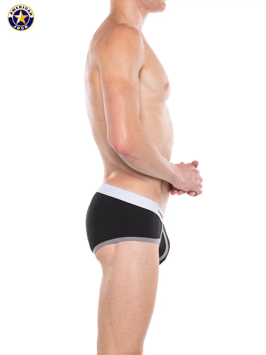 Side view of a male model wearing black brief underwear with white waistband and gray trim by AMERICAN JOCK