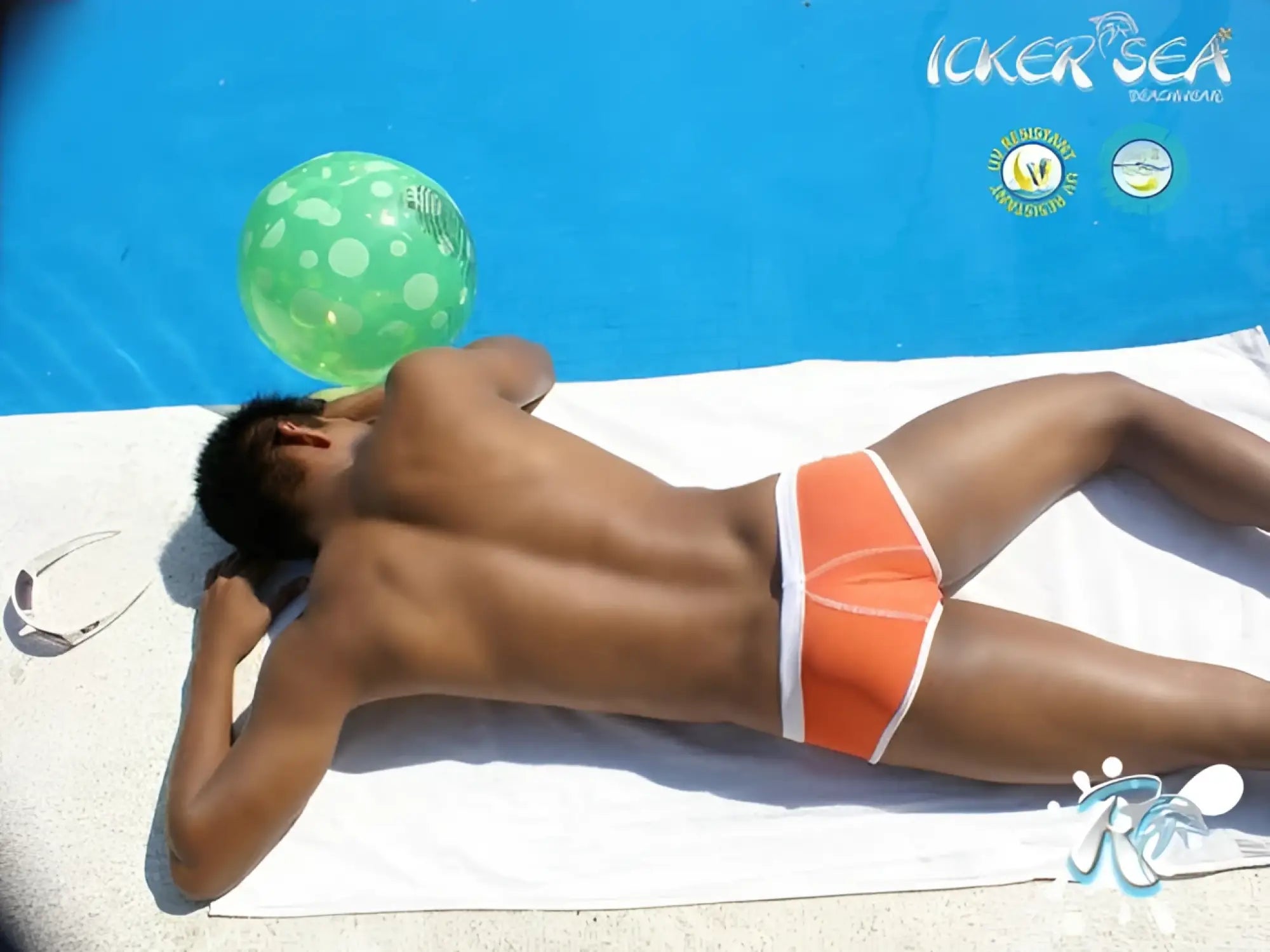 Orange swim trunks with white trim from icker sea cheeky mini bikini swimwear lying on towel beside pool