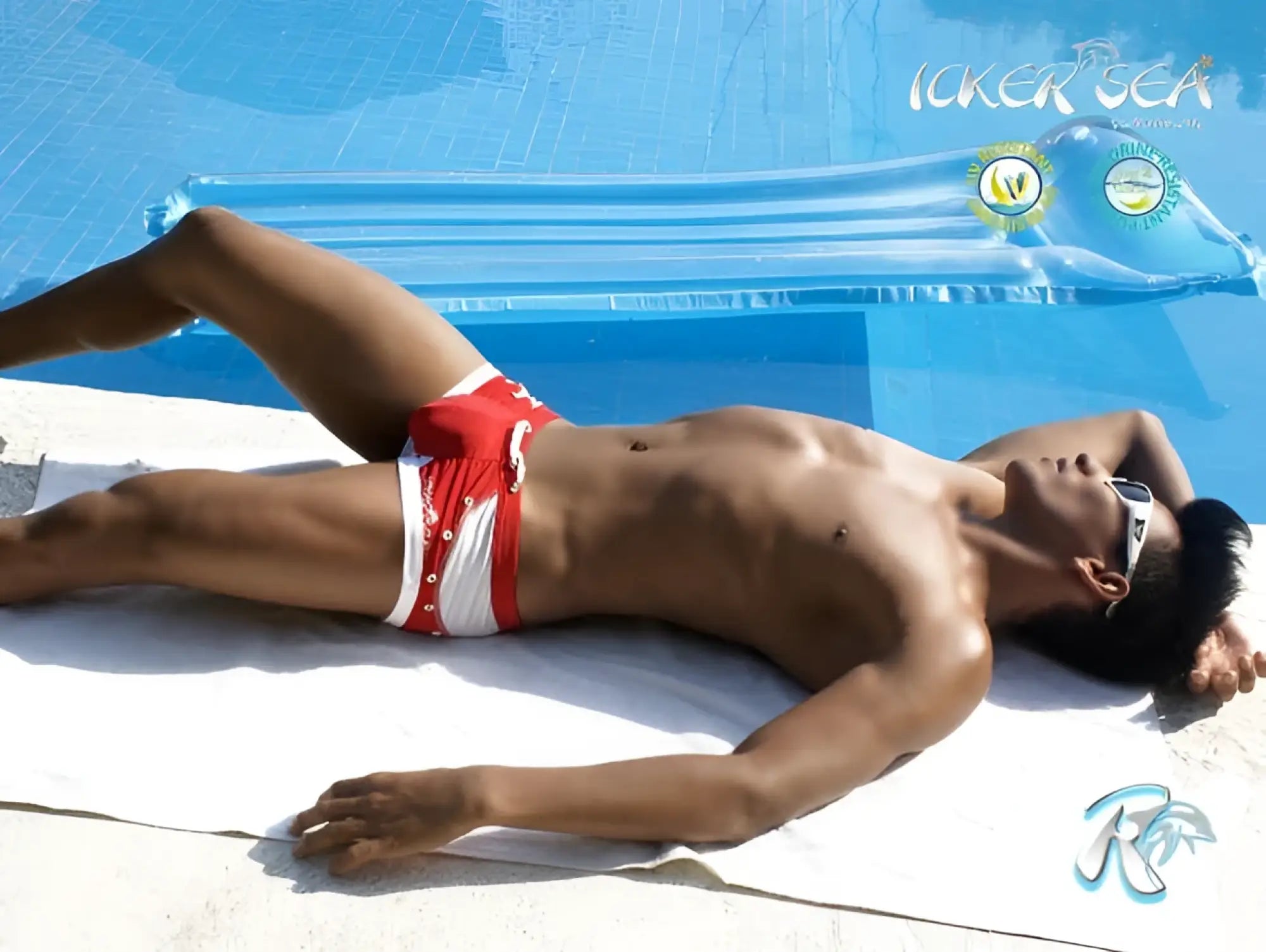 A man lies by the pool wearing icker sea eyelets square cut trunk swimwear in red with silver buttons