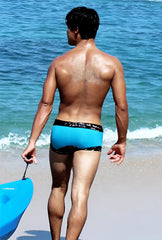 A man stands on the beach wearing Icker Sea lace up contrast square cut trunk swimwear in blue and black