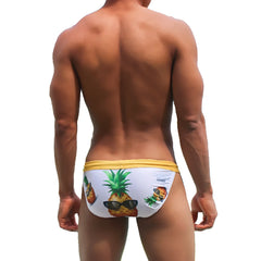 White swim trunks with yellow waistband and playful pineapple graphic wearing sunglasses for beachwear