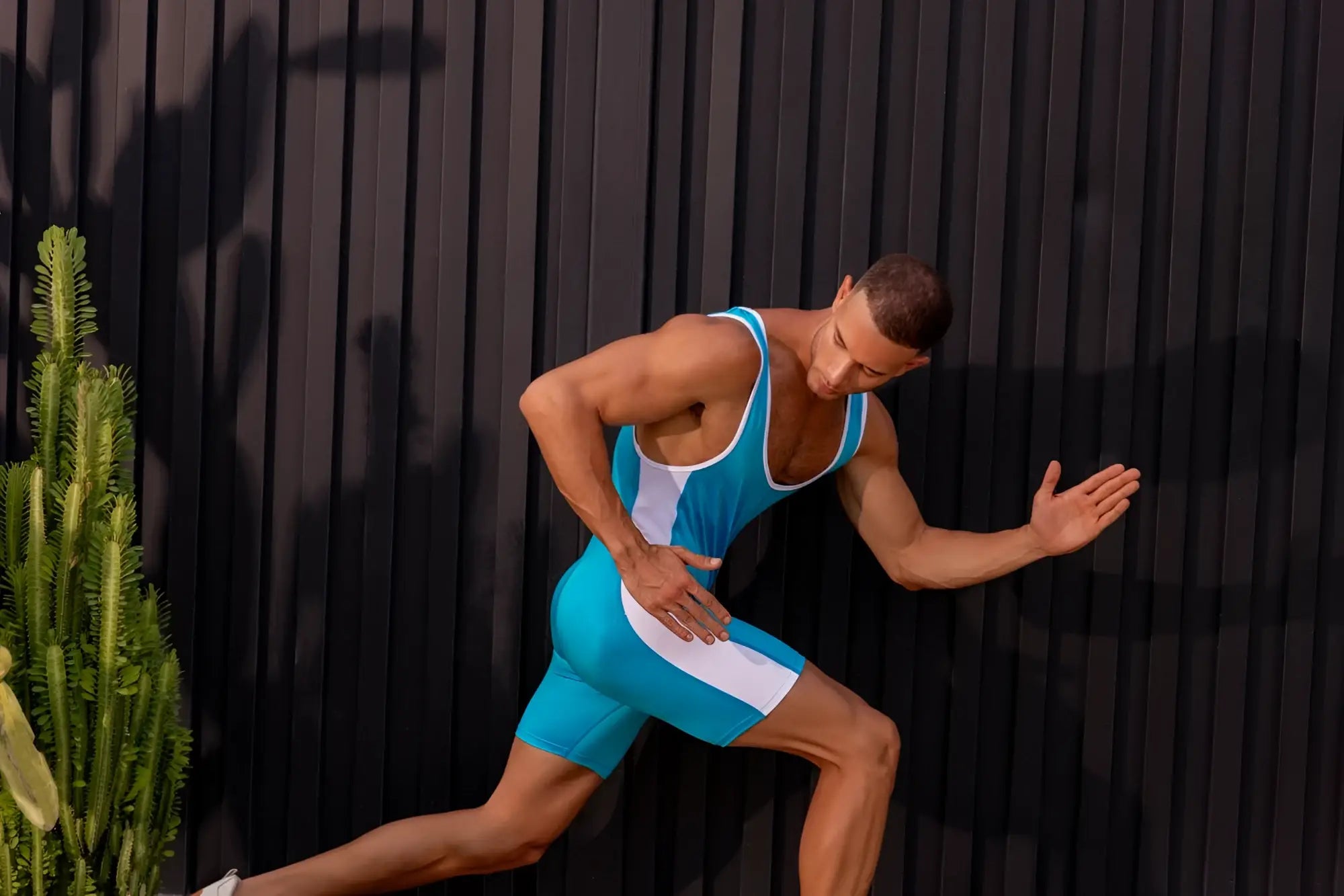 A muscular man wearing a turquoise jor 2216 fighter bodysuit with sleek seamless blue and white athletic material