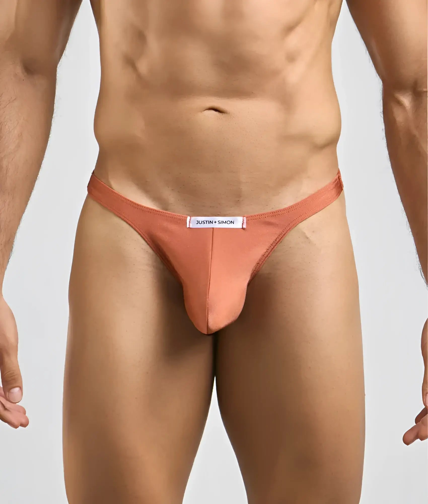 A sleek peach-colored justin simon classic tanga thong made of smooth form-fitting fabric with a branded waistband