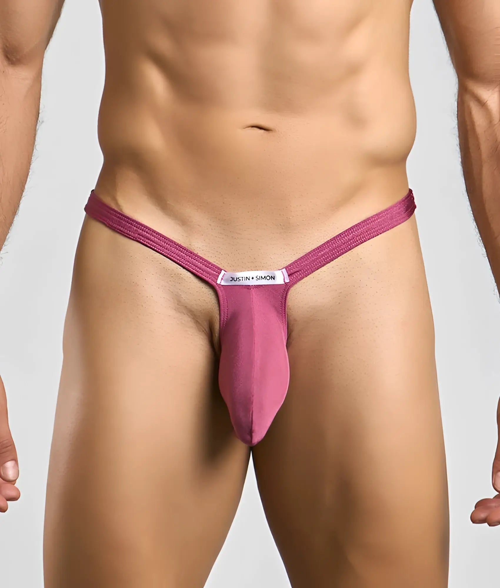 A magenta form-fitting thong with a central pouch and a white label featuring the justin + simon brand name