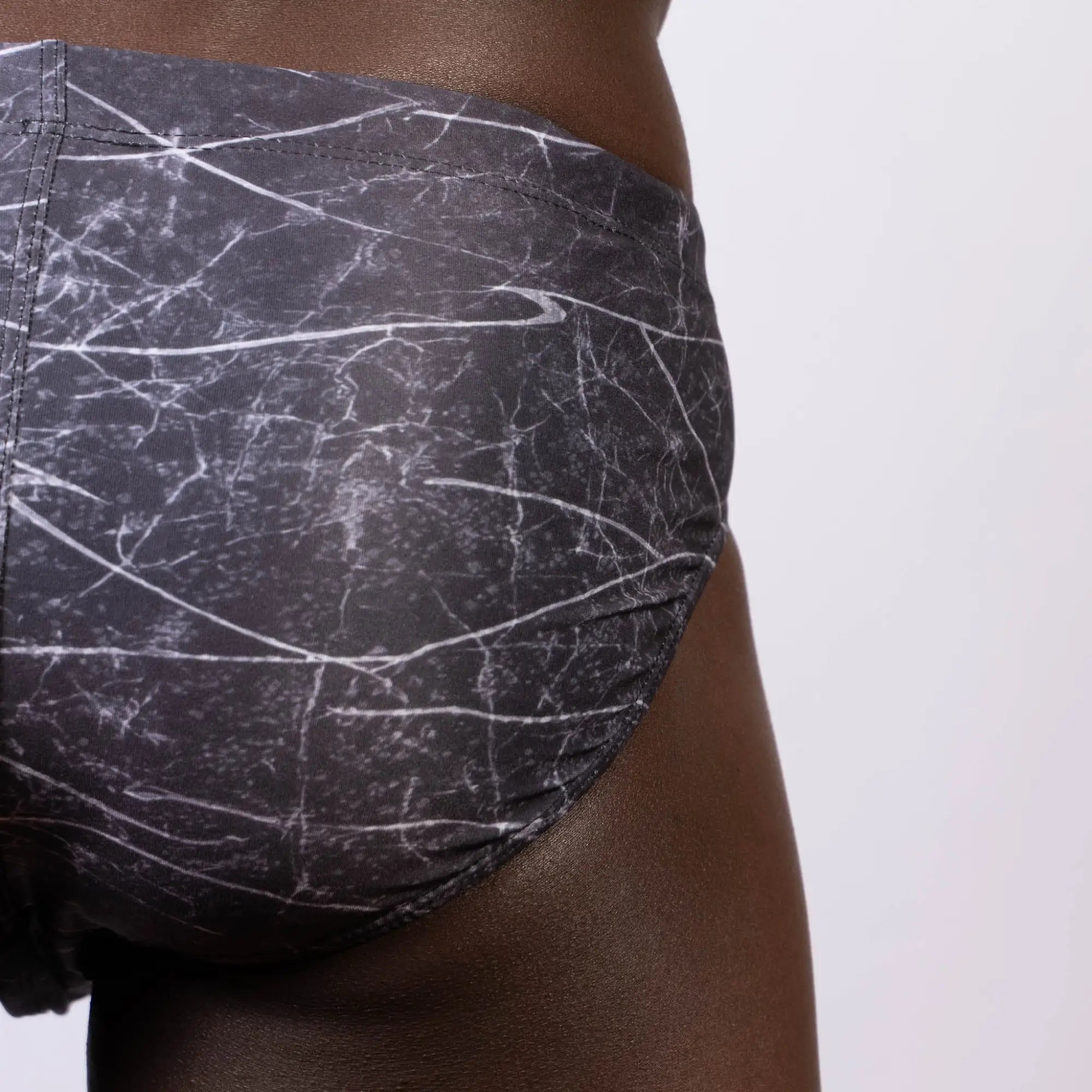 Black and white marble-patterned men’s lightning swim brief with subtle Nike swoosh logo in stretchy fabric