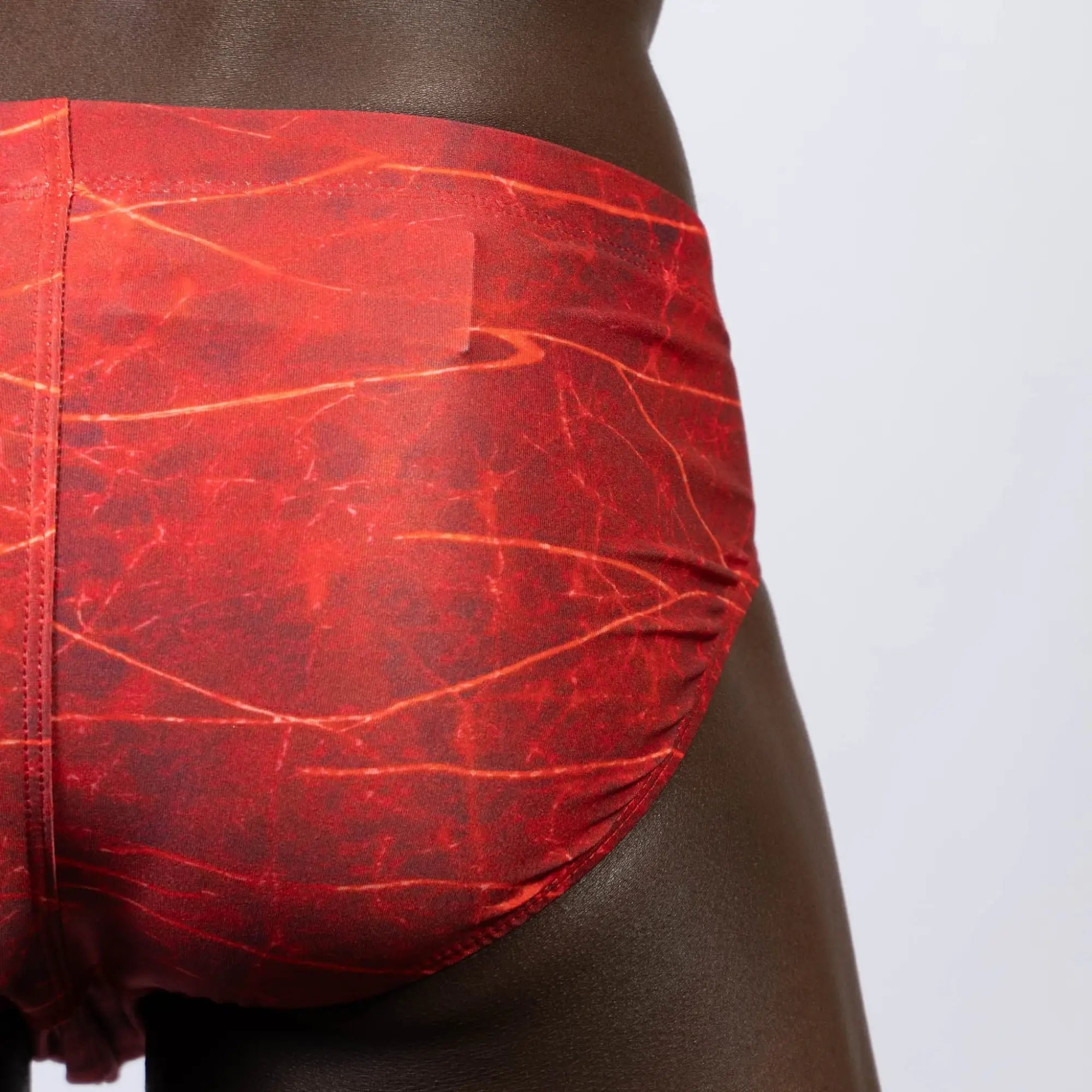 Lightning swim brief in red with a marbled pattern and subtle orange veining designed for swimming and beachwear