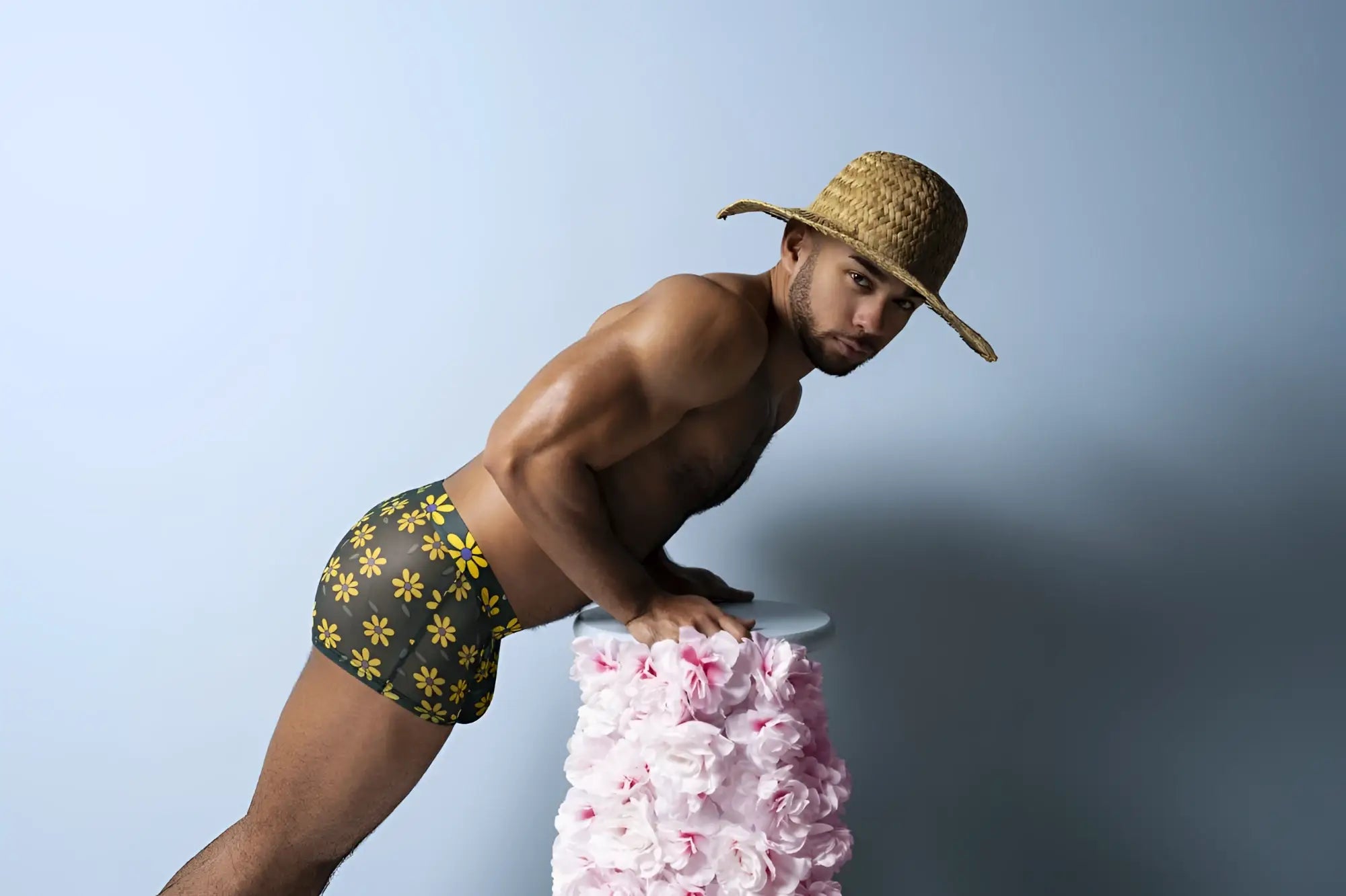 A man wearing male power petal power pouch shorts in black with yellow daisy print and a straw hat