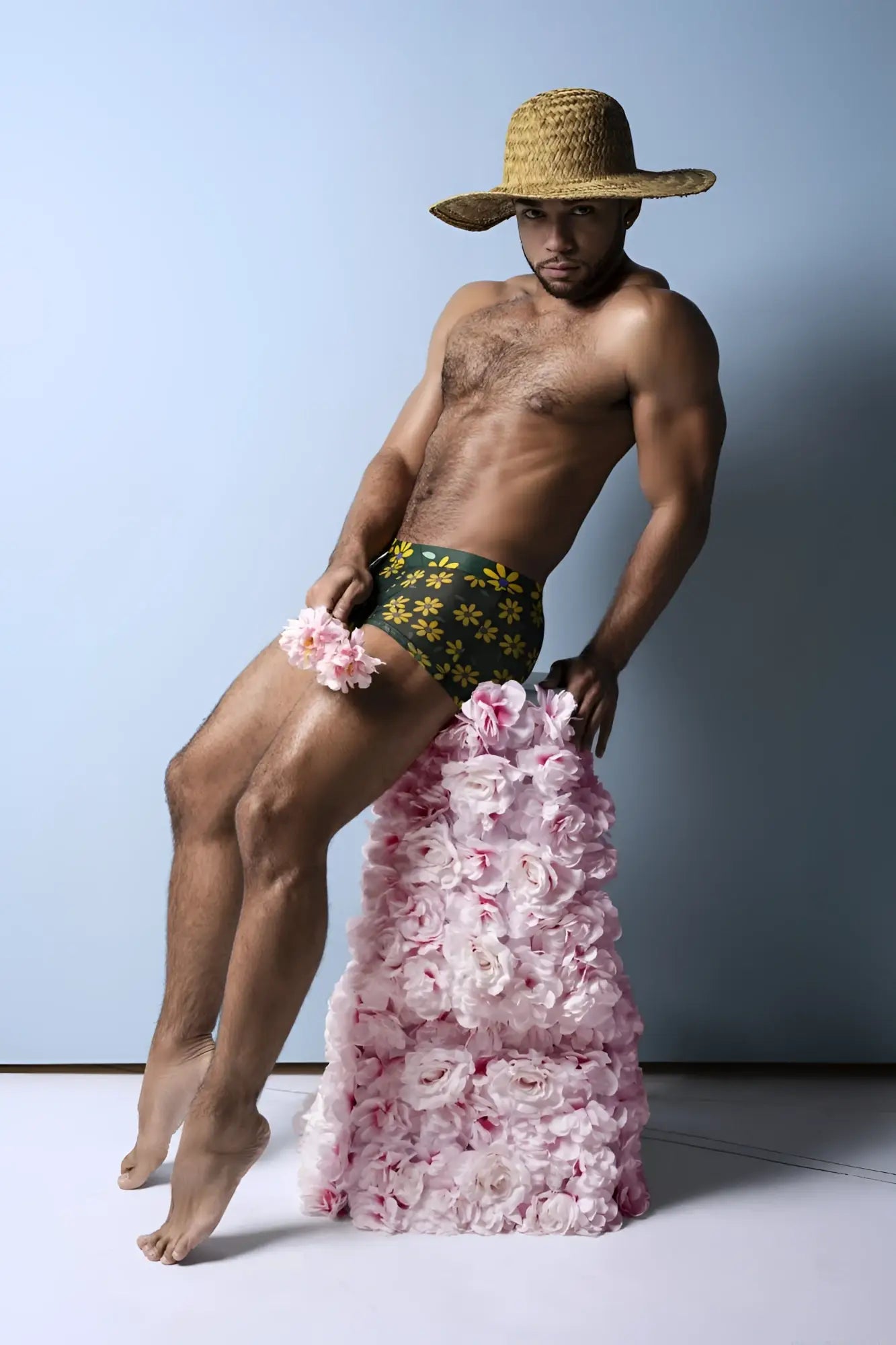 A man wearing male power daisy print petal power pouch shorts in green floral pattern with pink roses down his legs