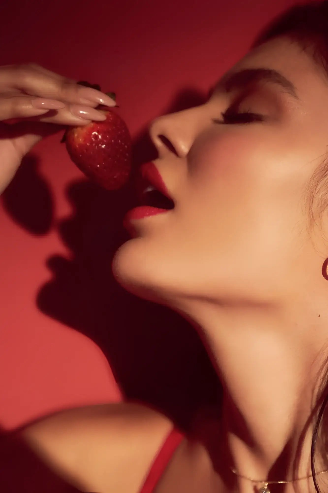 A hand with manicured nails holding a ripe red strawberry wearing the mapale 8899 black-red two piece set