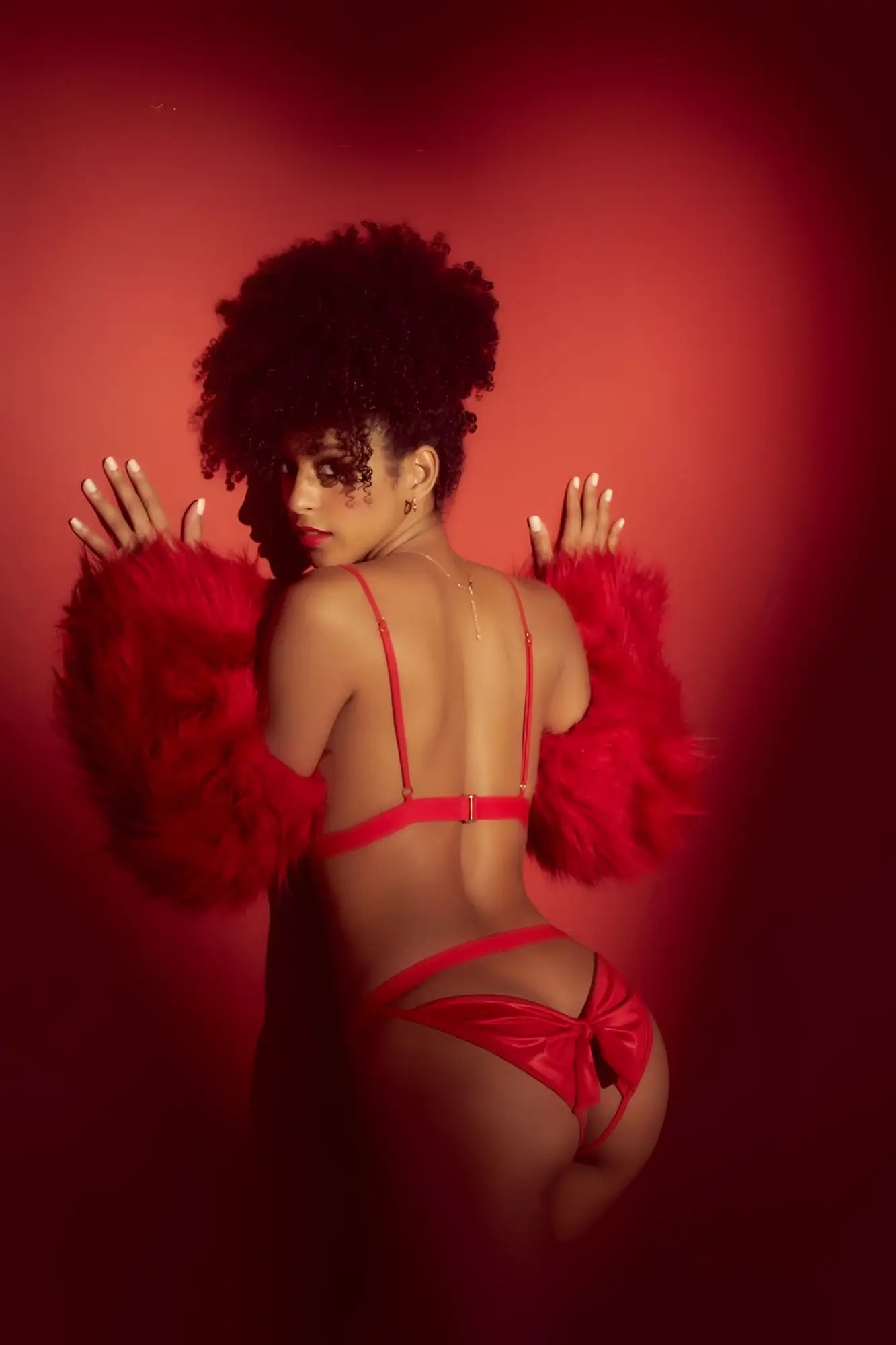 A woman wearing a vibrant red satin lingerie two piece set with thin straps and a matching feathered arm accessory