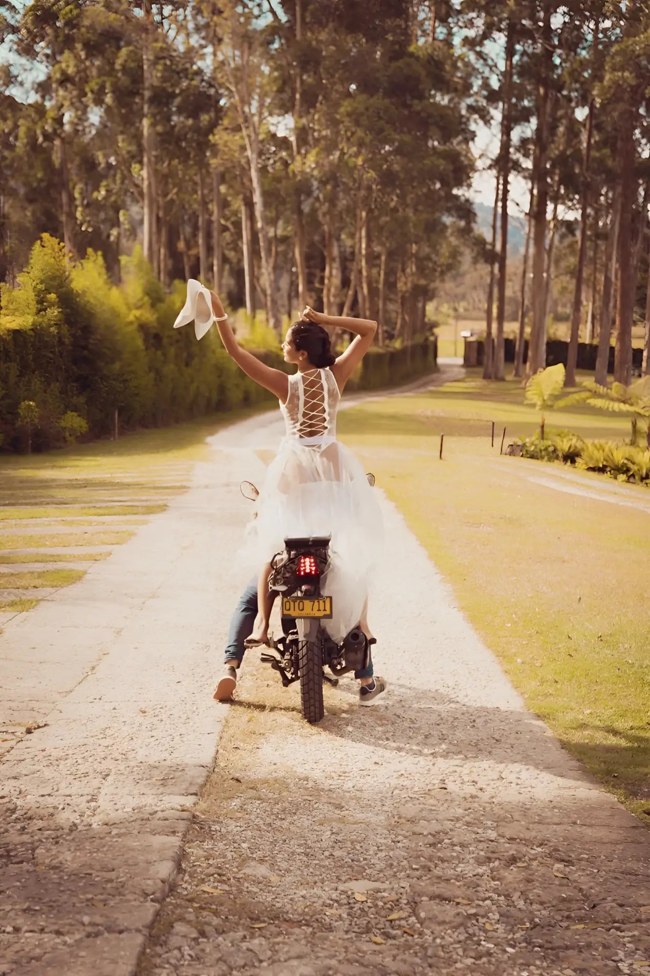 A bride wearing the back of a white lace Mapale 8932 teddy with open back and veil riding a motorcycle
