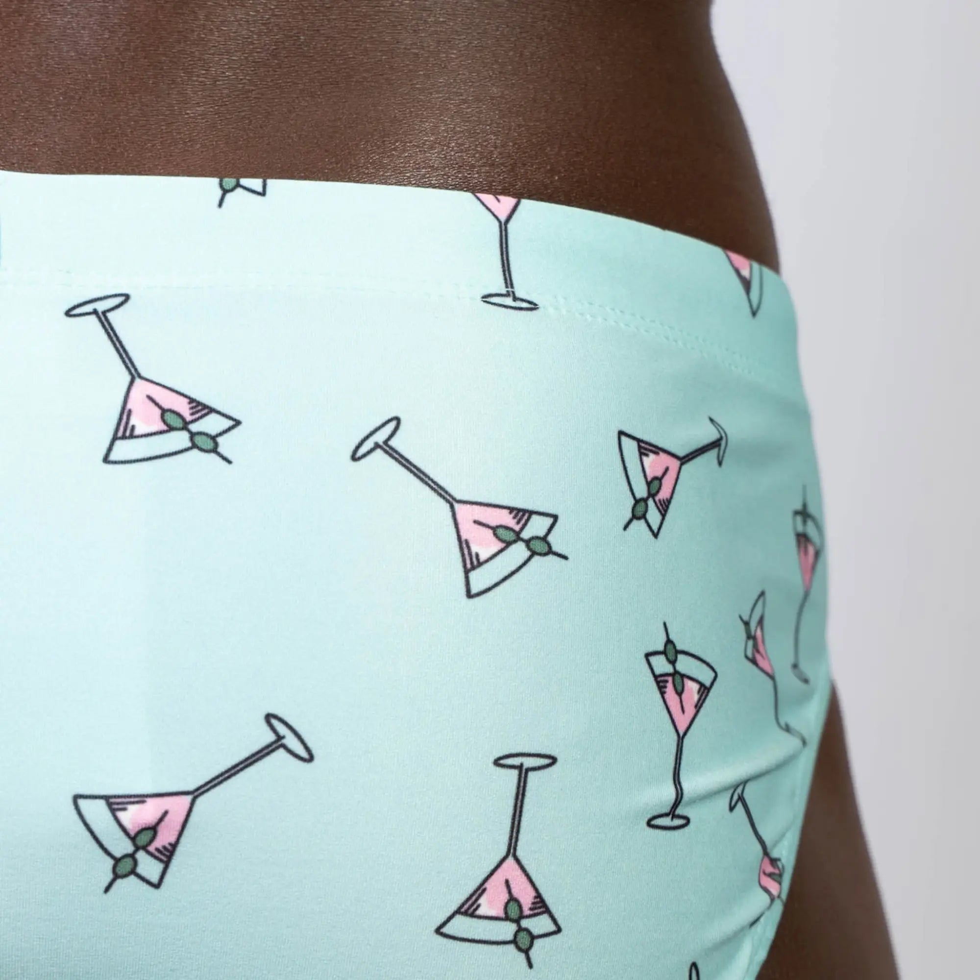 Mint green martini swim brief with playful pink martini glass pattern and olive garnishes in black outline