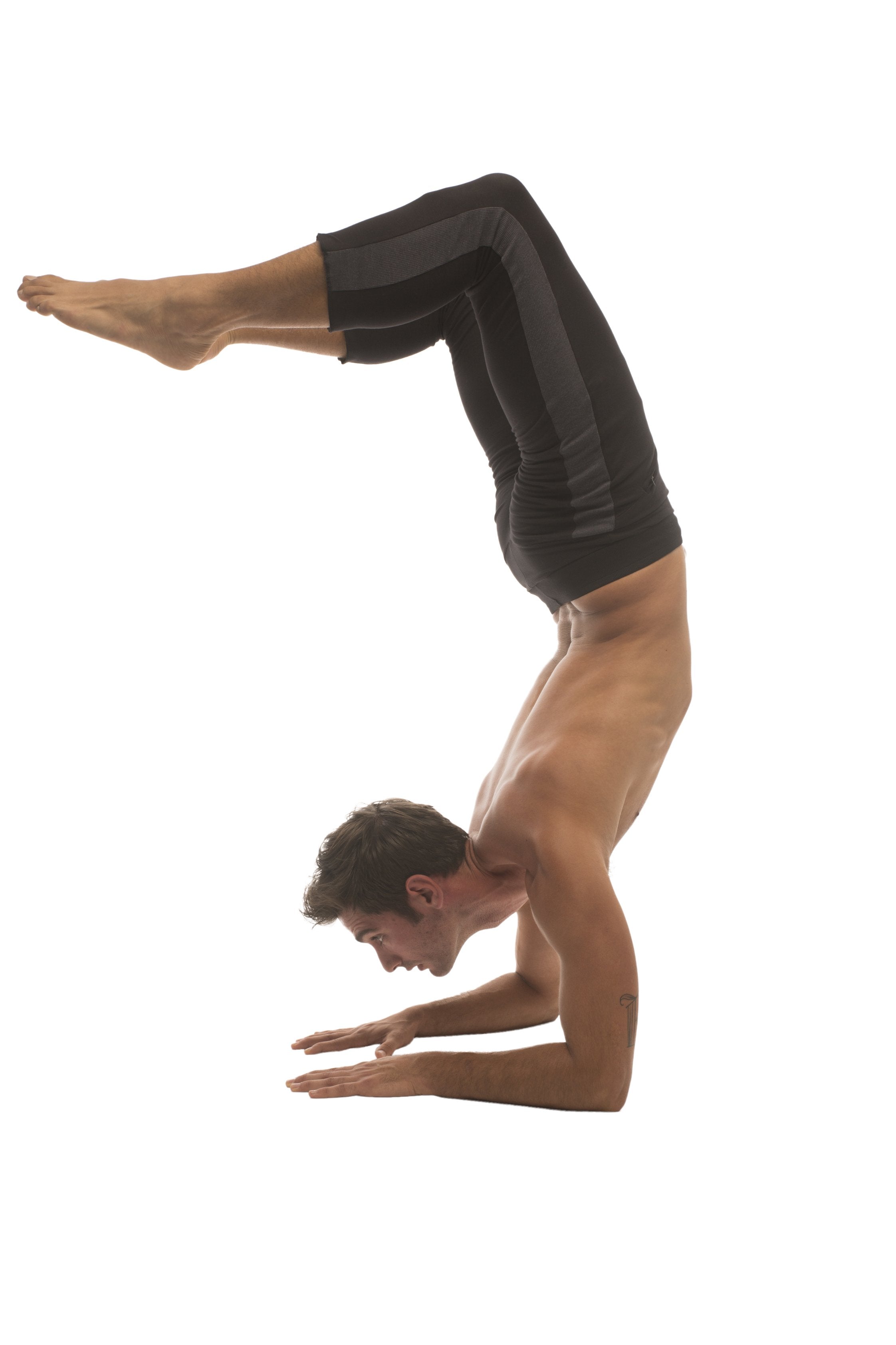 A man wearing black 4/5 zipper pocket capri yoga pants performs a handstand in form-fitting athletic leggings