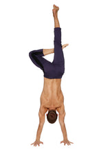 A man wearing mens 4/5 zipper pocket capri yoga pants eggplant with black and charcoal performing a handstand