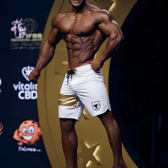 White metromusclewear gold physique board shorts with gold stripe black drawstring and shield logo on left leg