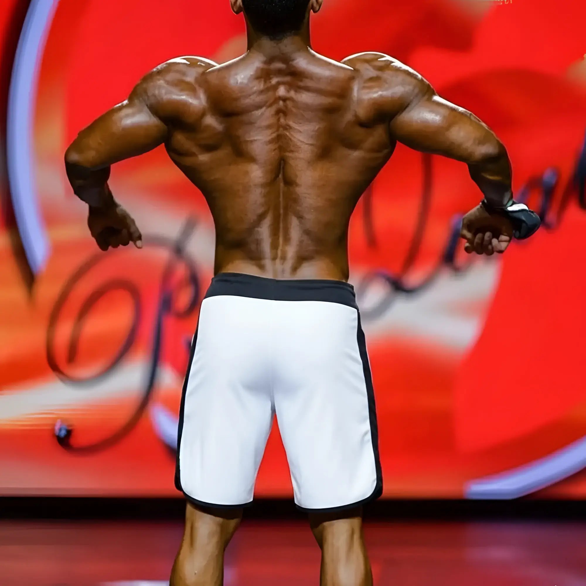 Back view of a muscular man wearing white athletic metro musclewear ifbb pro mens physique board shorts with black trim