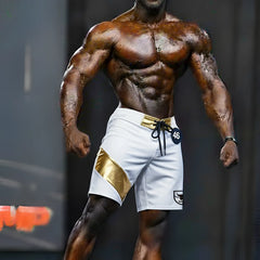White MetroMaleWear Physique board shorts with gold diagonal stripe, matching belt loop, black drawstring, and logo patch