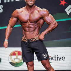 Black MetroMaleWear Physique board shorts with leopard-print waistband and white shield logo on lower left leg