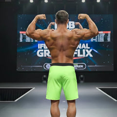 A muscular man on stage wearing MetroMaleWear Physique board shorts in lime green with a black waistband