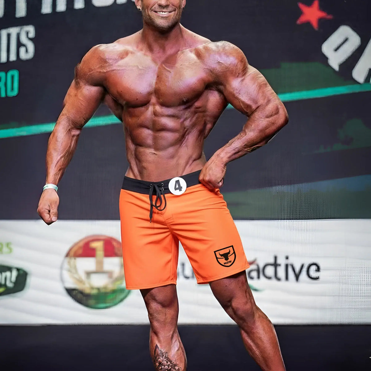MetroMaleWear physique board short orange with black waistband and drawstring featuring a shield logo on the lower right leg