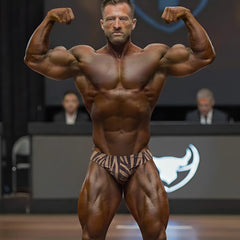 A muscular man flexing on stage wearing MetroMaleWear gold zebra posing suit in brown and beige zebra-striped briefs