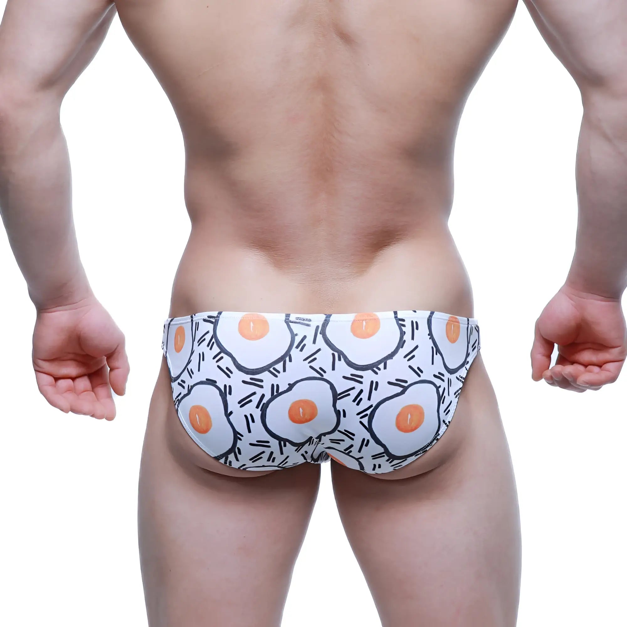 White swim trunks by metromalewear featuring a playful cartoon-style fried egg pattern with orange yolks and black outlines