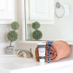 Blue and black five-blade disposable razor resting on a rolled terracotta towel with mixologie manscaping cream shave