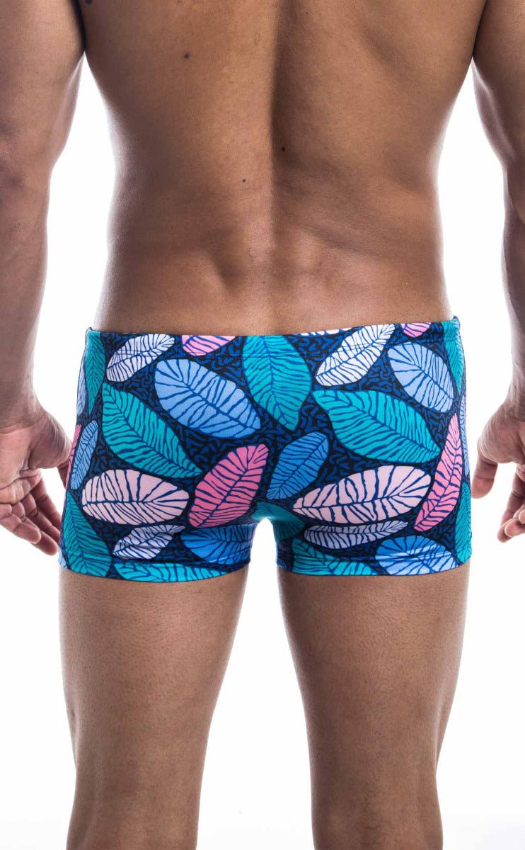 Oceanico square cut swim trunks with vibrant teal pink and white tropical leaf pattern on dark blue base